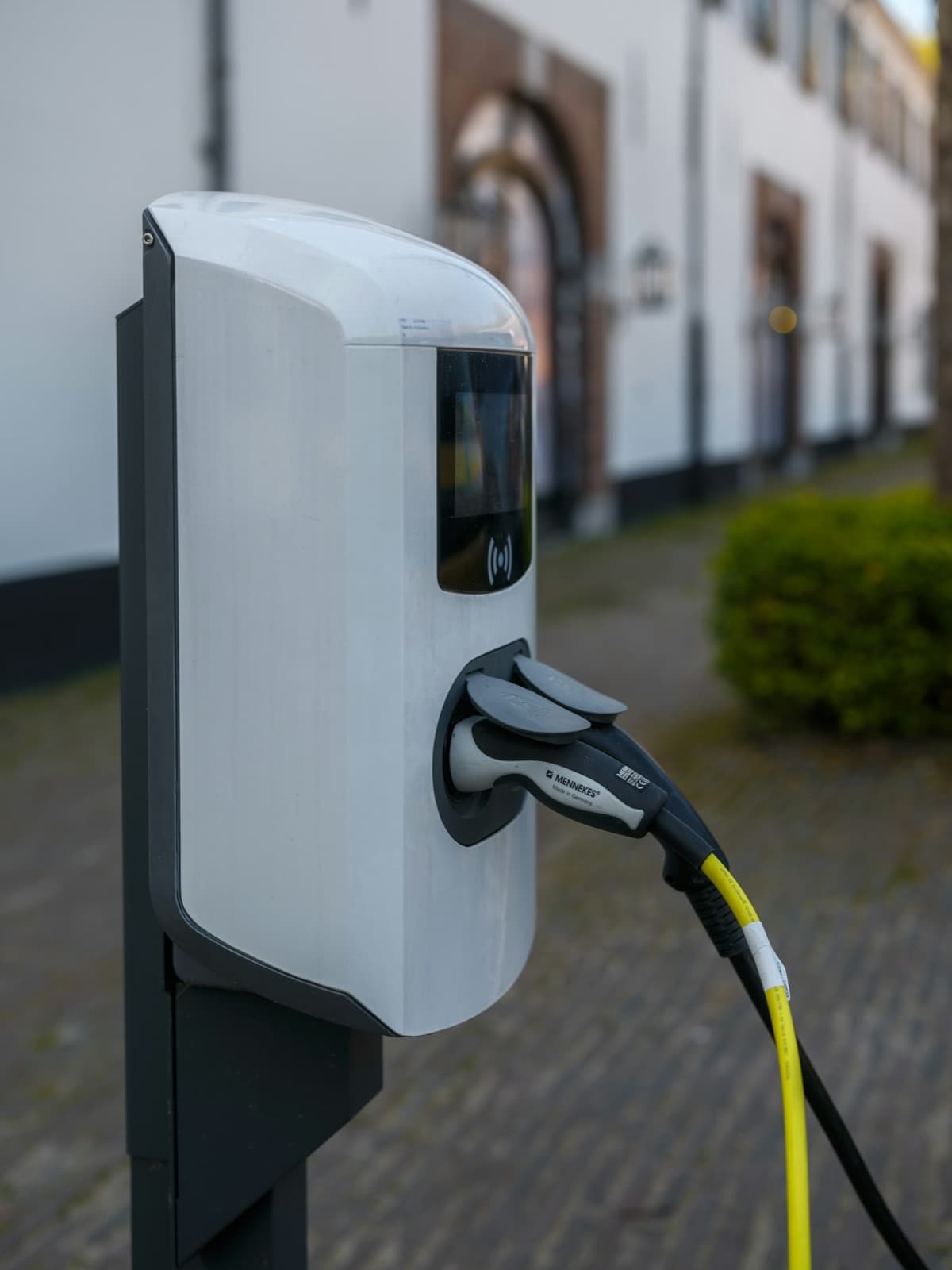 Estação de recarga para carro elétrico com o conector plugado e cabo amarelo, em uma rua de calçamento